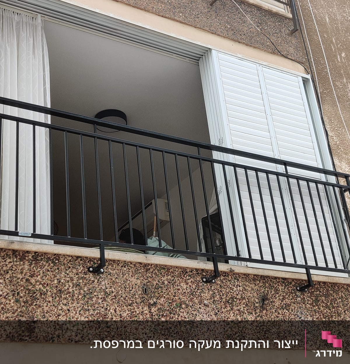 מעקה מתכת שחור על מרפסת עם תריסים פתוחים